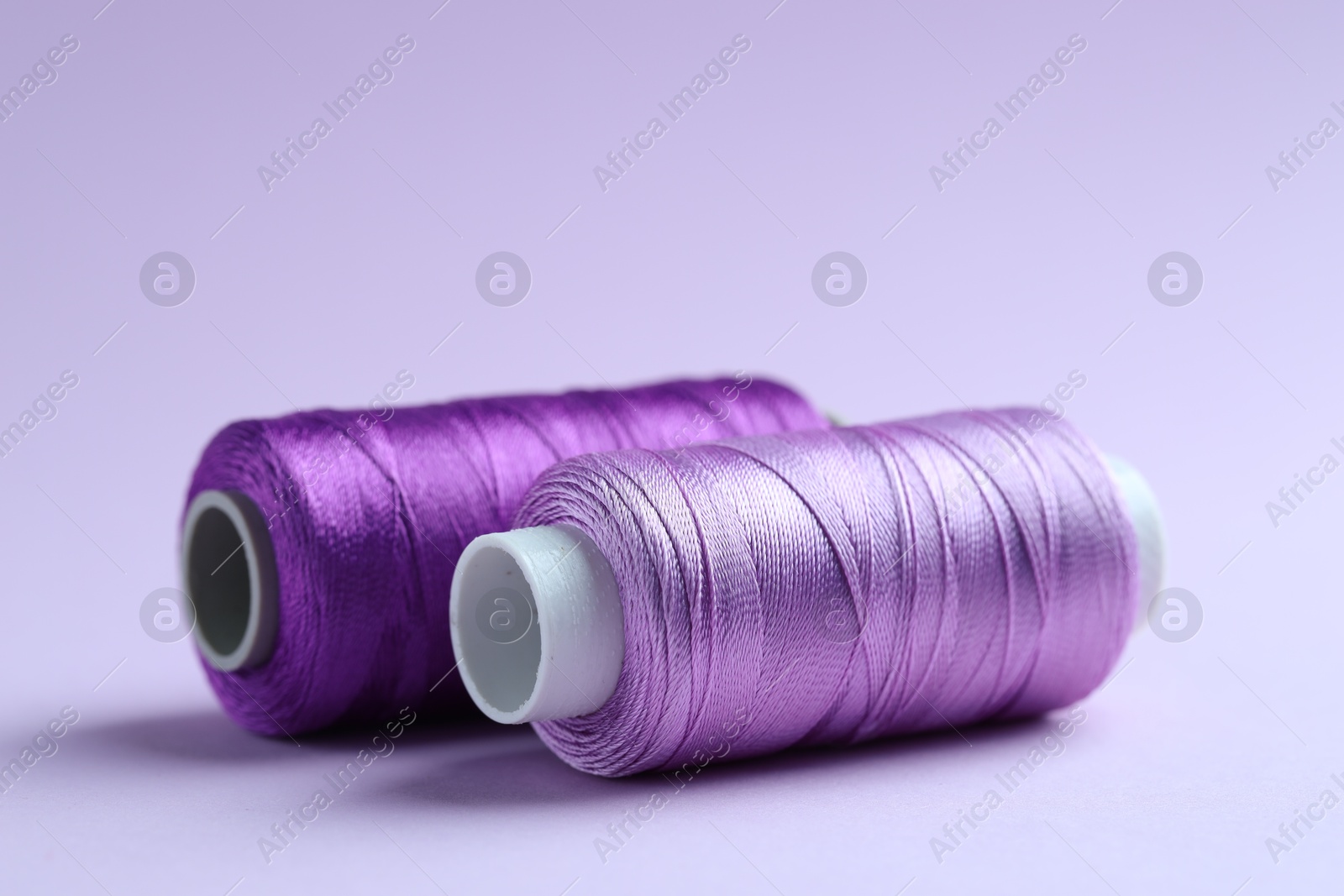 Photo of Spools of colorful sewing threads on lilac background, closeup