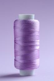 Photo of Spool of violet sewing thread on lilac background