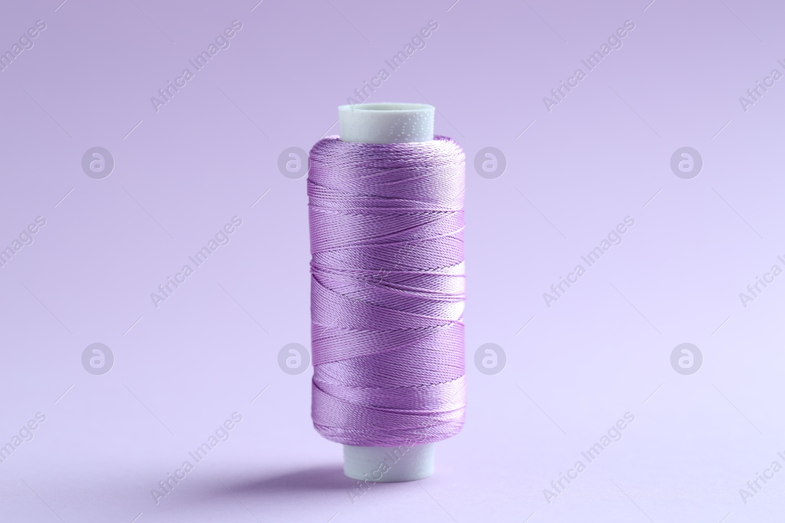 Photo of Spool of violet sewing thread on lilac background