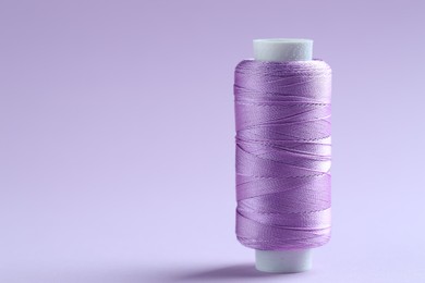 Photo of Spool of violet sewing thread on lilac background, space for text