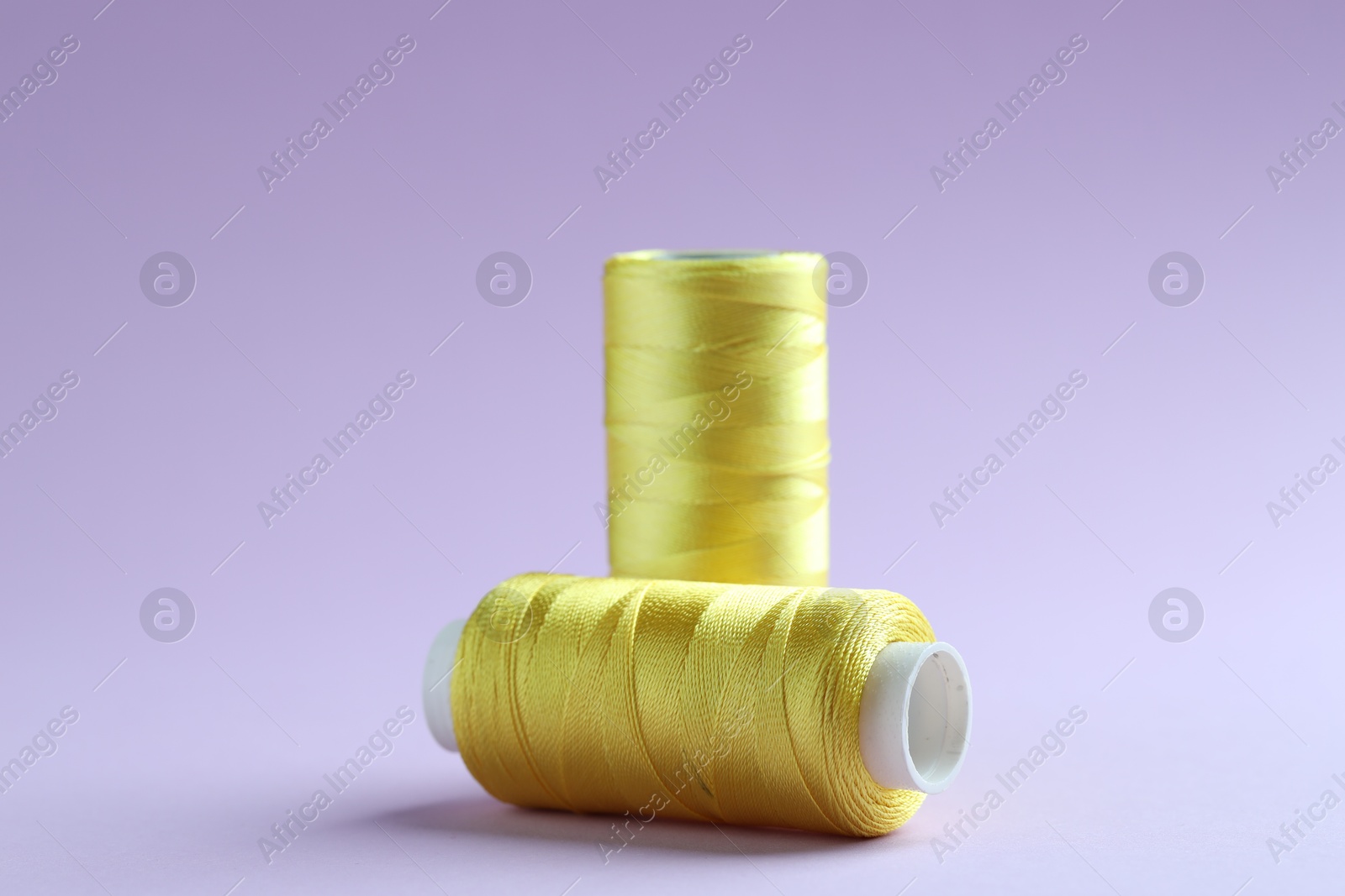 Photo of Spools of yellow sewing threads on lilac background