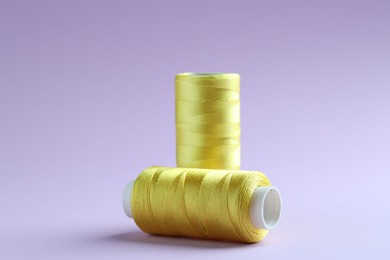 Photo of Spools of yellow sewing threads on lilac background