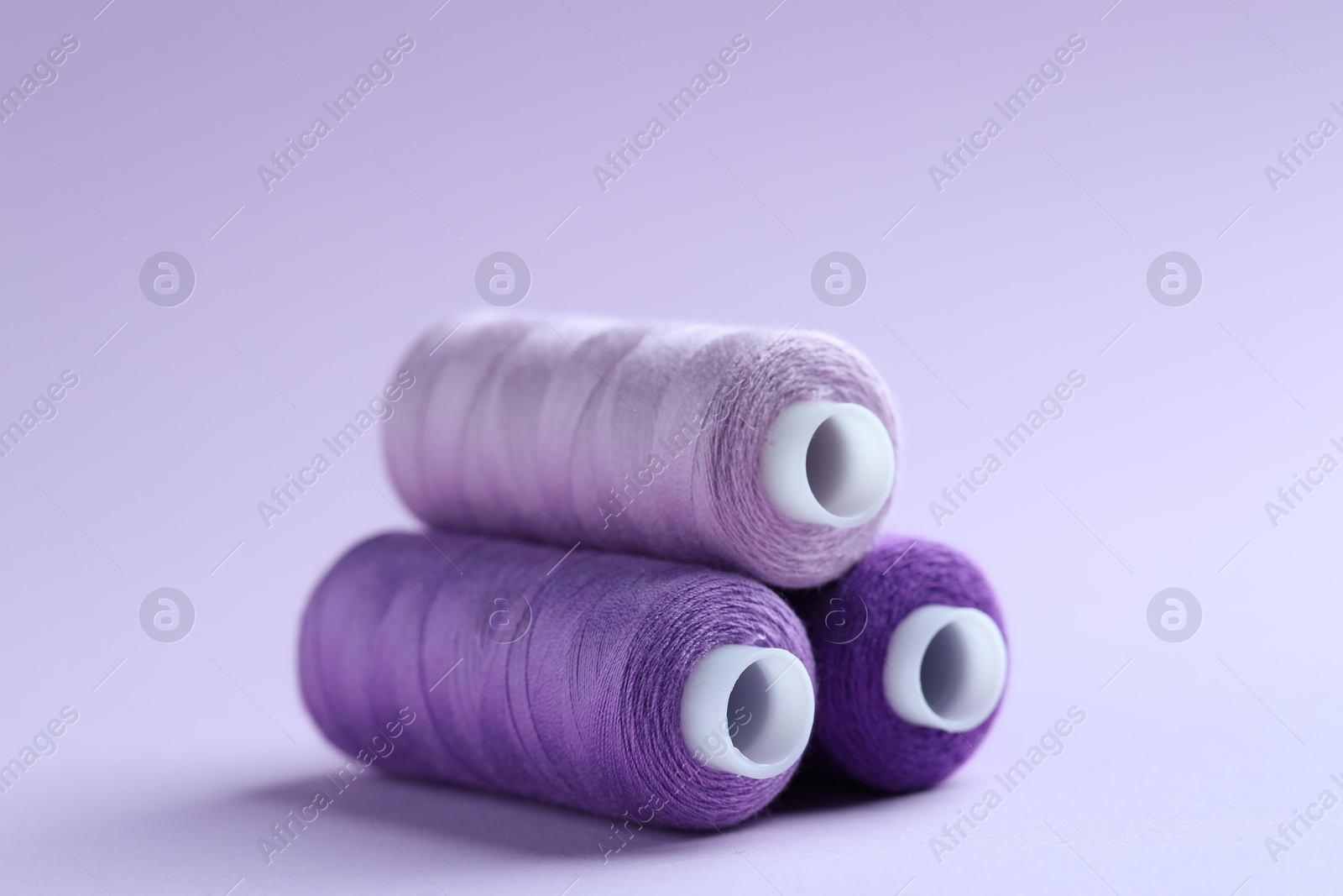 Photo of Spools of colorful sewing threads on lilac background, closeup