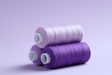 Photo of Spools of colorful sewing threads on lilac background, closeup