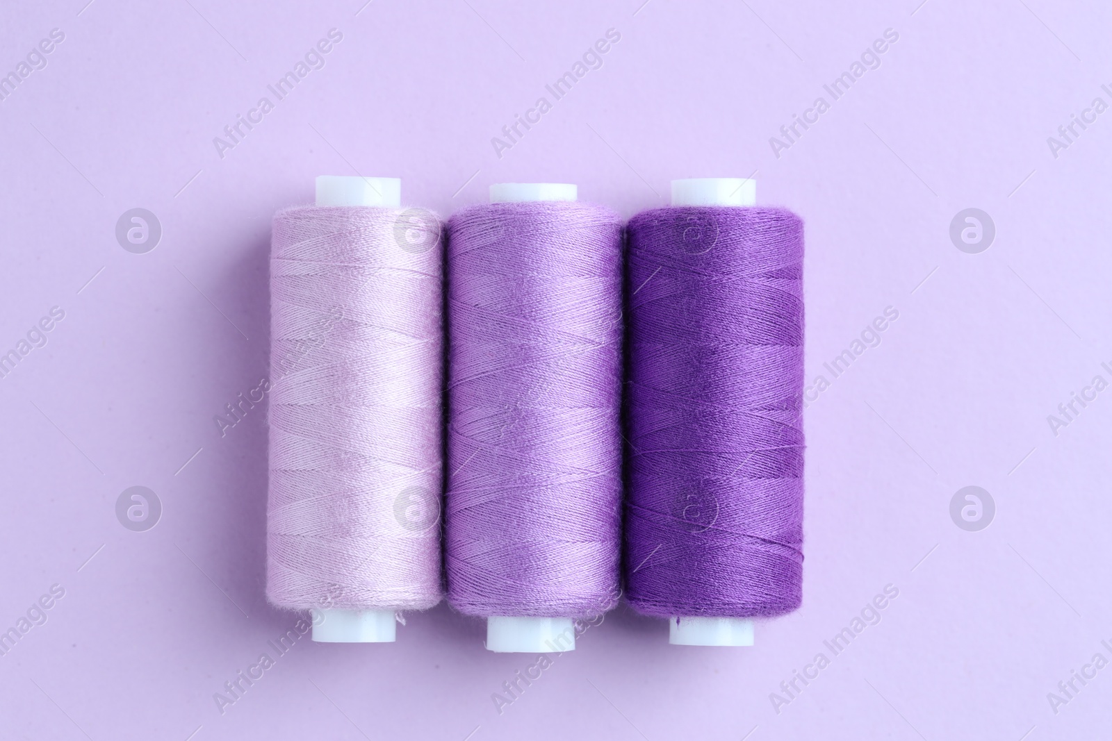 Photo of Spools of colorful sewing threads on lilac background, flat lay