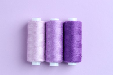 Photo of Spools of colorful sewing threads on lilac background, flat lay