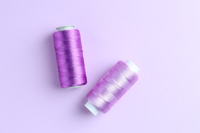 Photo of Spools of colorful sewing threads on lilac background, top view