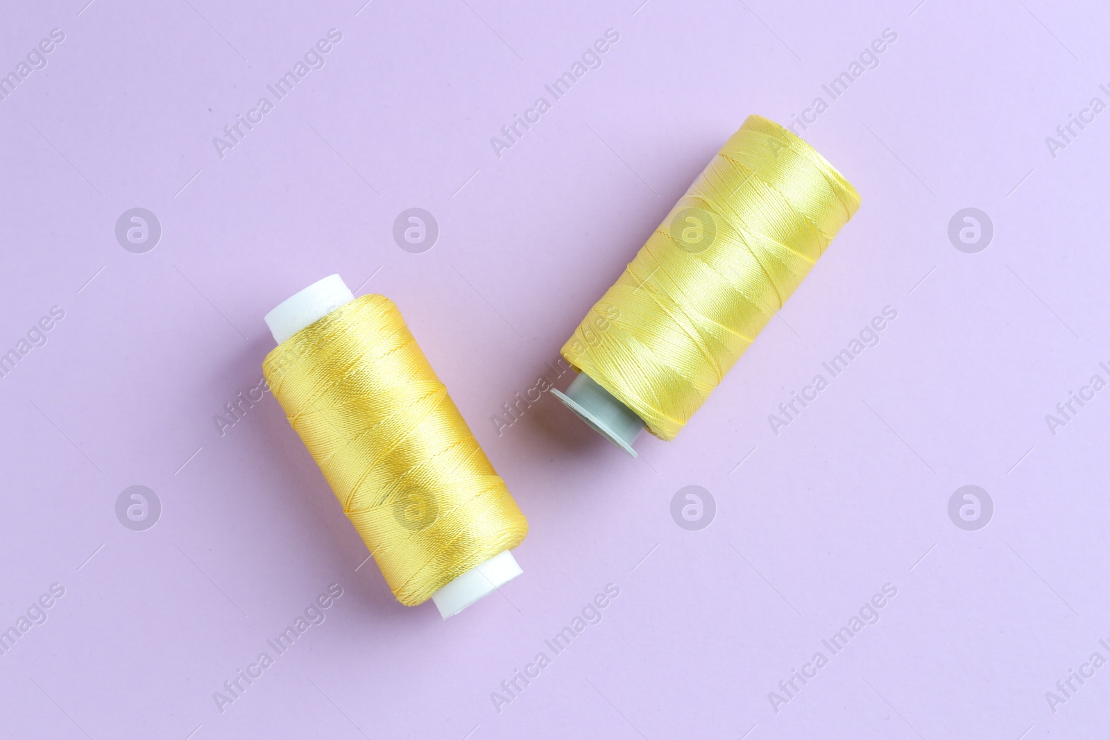 Photo of Spools of yellow sewing threads on lilac background, top view