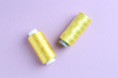 Photo of Spools of yellow sewing threads on lilac background, top view