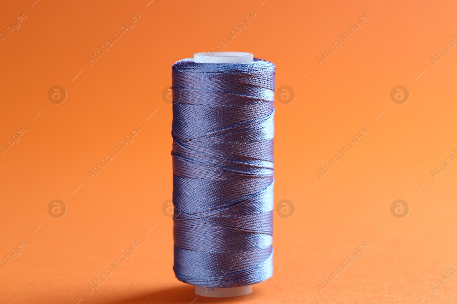 Photo of Spool of blue sewing thread on orange background