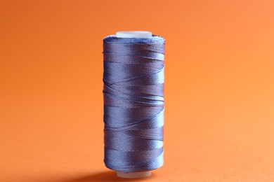 Photo of Spool of blue sewing thread on orange background