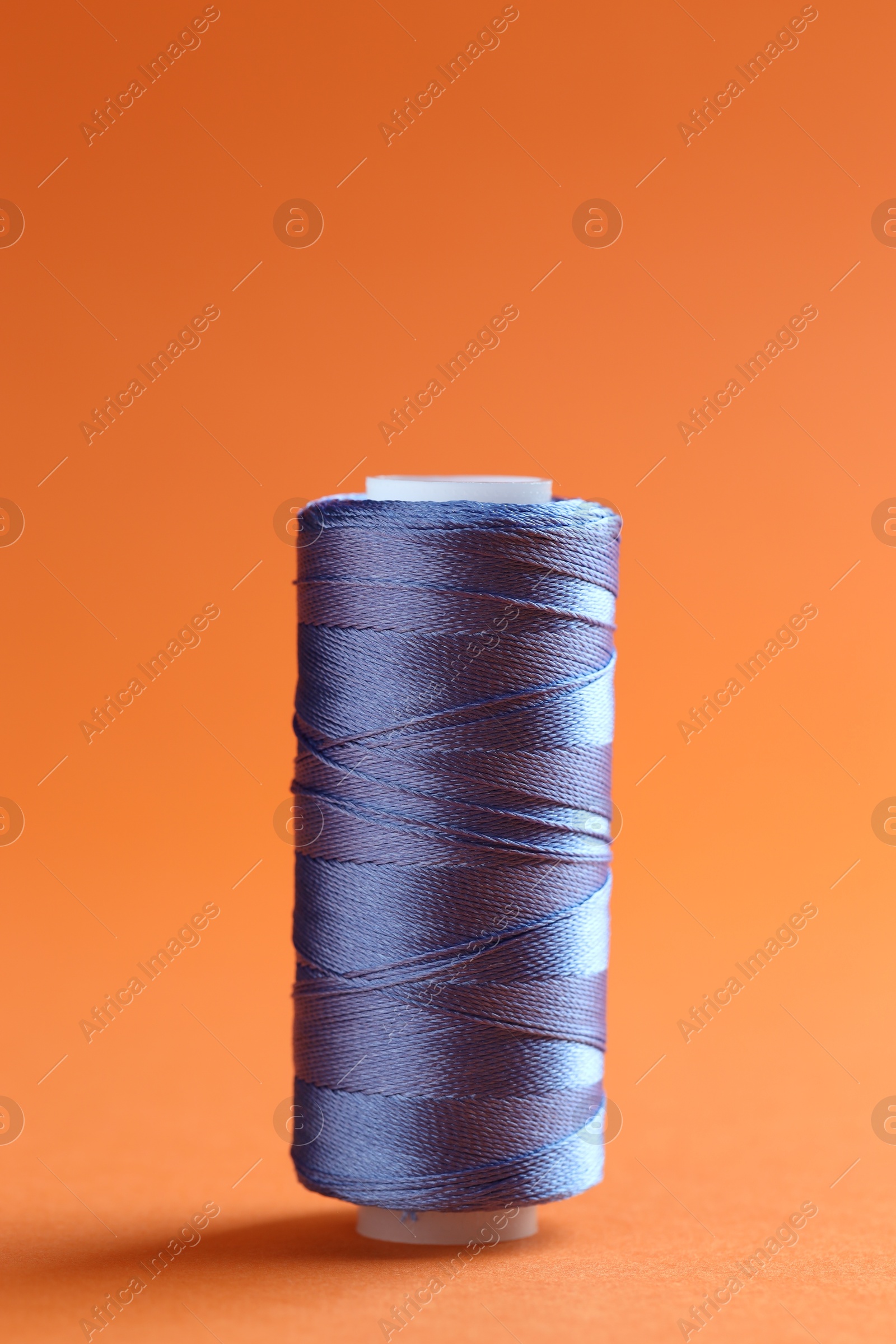 Photo of Spool of blue sewing thread on orange background