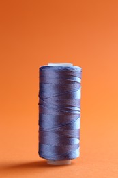 Photo of Spool of blue sewing thread on orange background