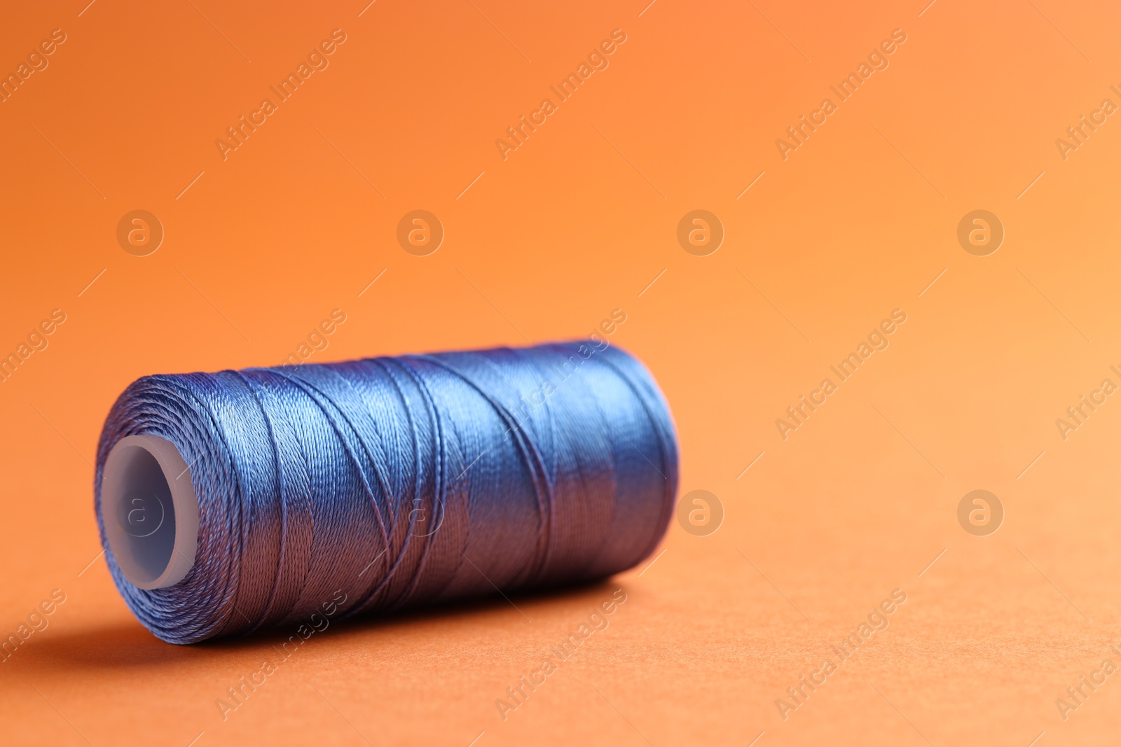 Photo of Spool of blue sewing thread on orange background, closeup. Space for text