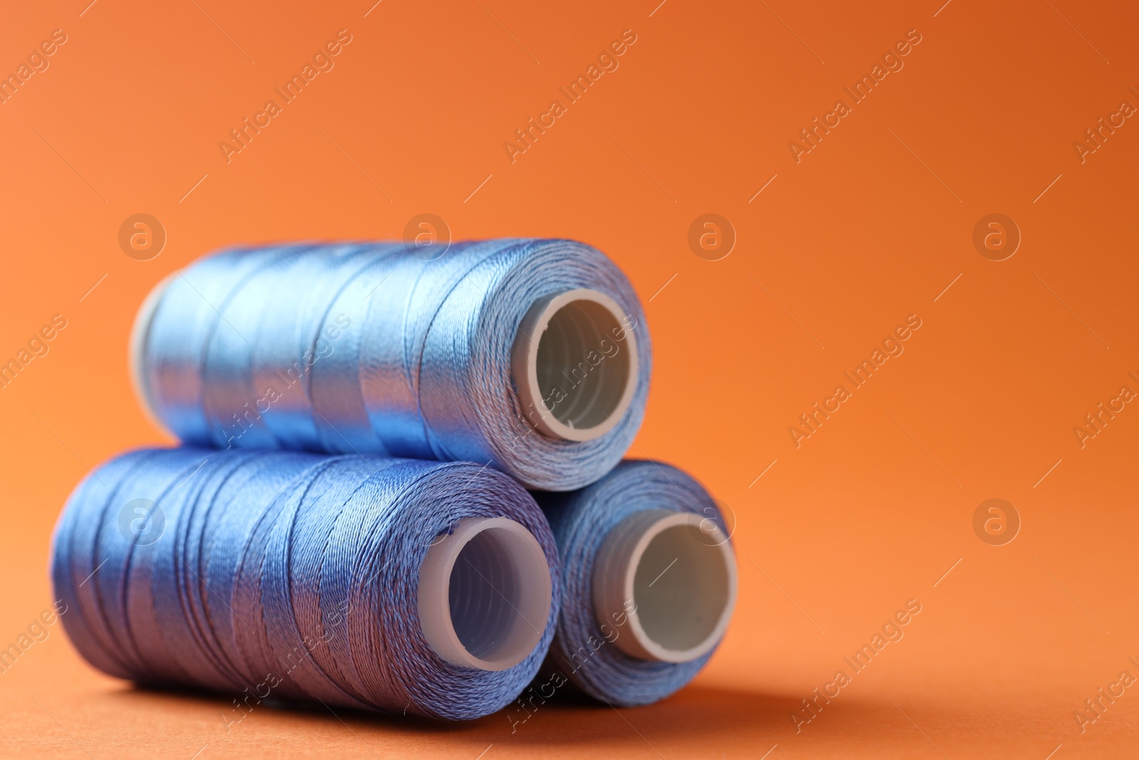 Photo of Spools of sewing threads on orange background, closeup. Space for text