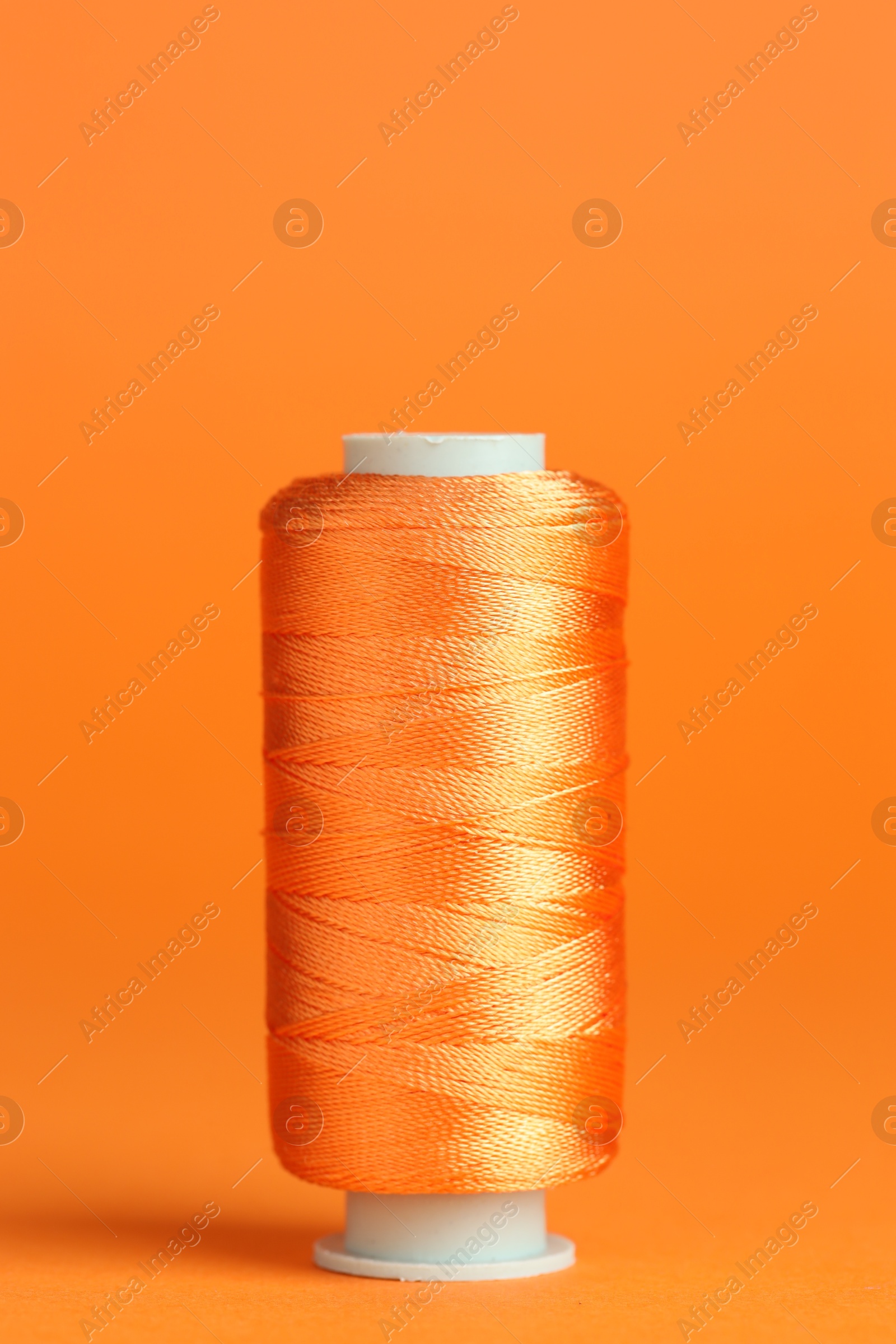 Photo of Spool of sewing thread on orange background