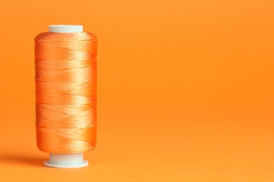 Photo of Spool of sewing thread on orange background