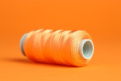 Photo of Spool of sewing thread on orange background, closeup