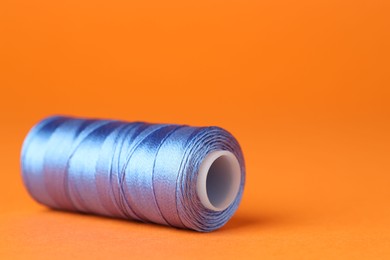 Photo of Spool of blue sewing thread on orange background, closeup. Space for text