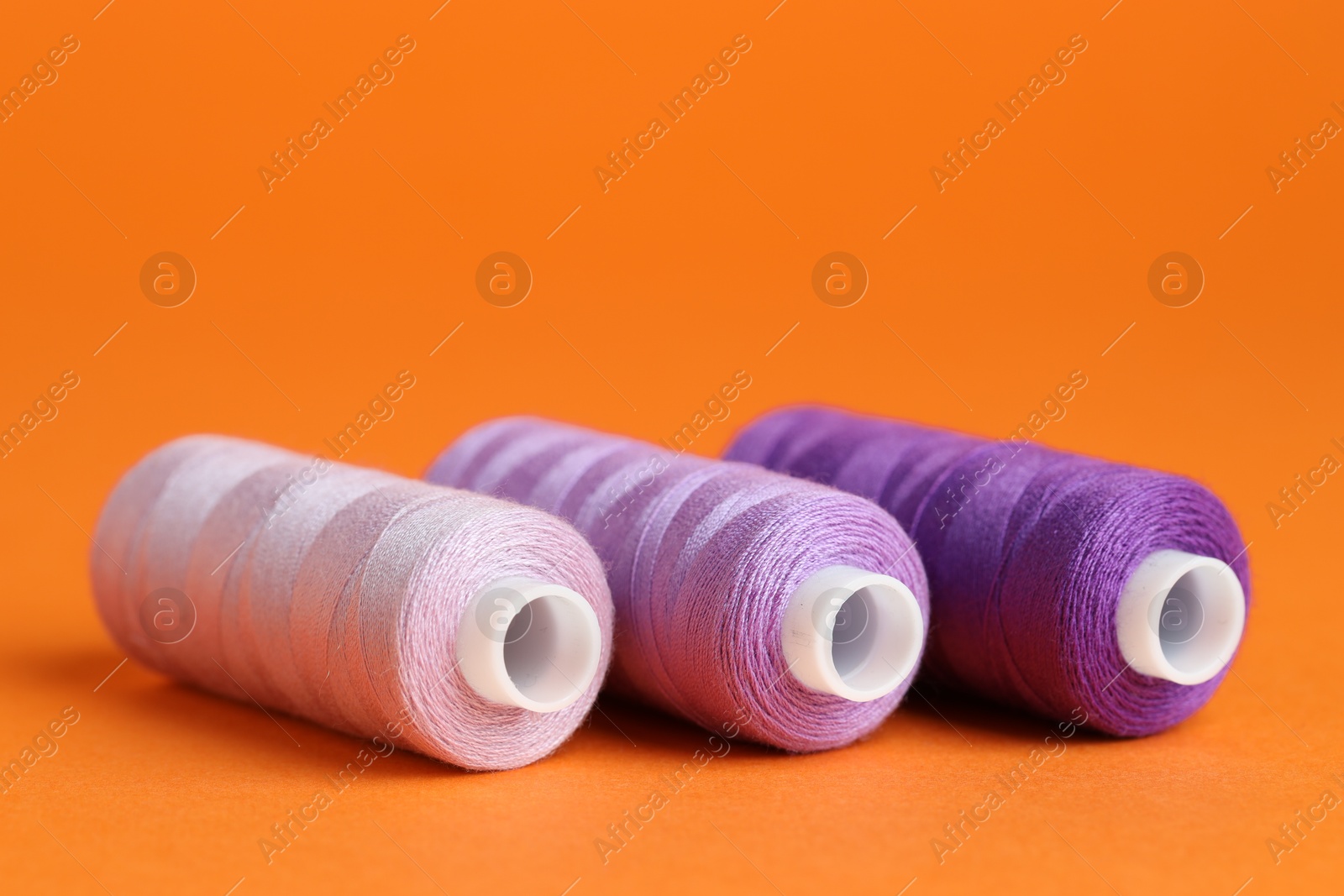 Photo of Spools of colorful sewing threads on orange background, closeup