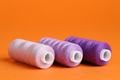 Photo of Spools of colorful sewing threads on orange background, closeup