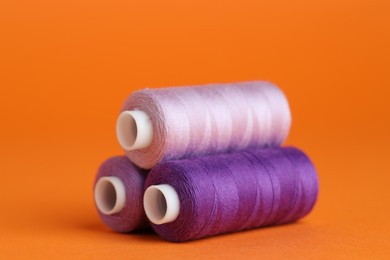 Photo of Spools of colorful sewing threads on orange background, closeup