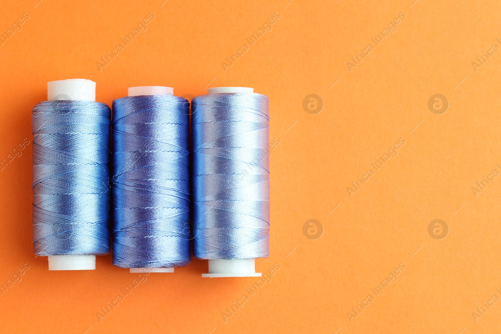 Photo of Spools of colorful sewing threads on orange background, flat lay. Space for text