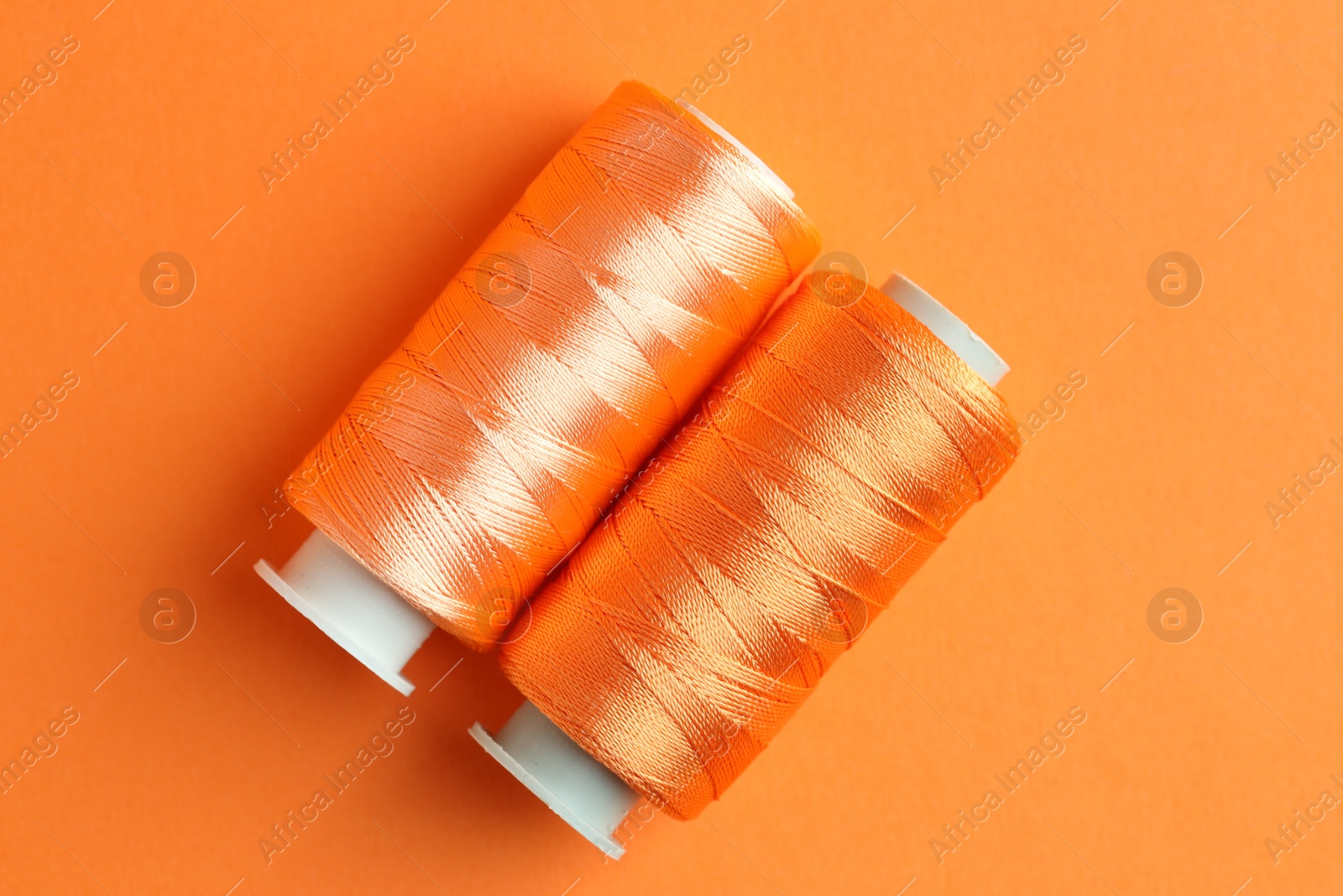 Photo of Spools of bright sewing threads on orange background, top view