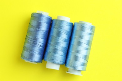 Photo of Spools of colorful sewing threads on yellow background, flat lay