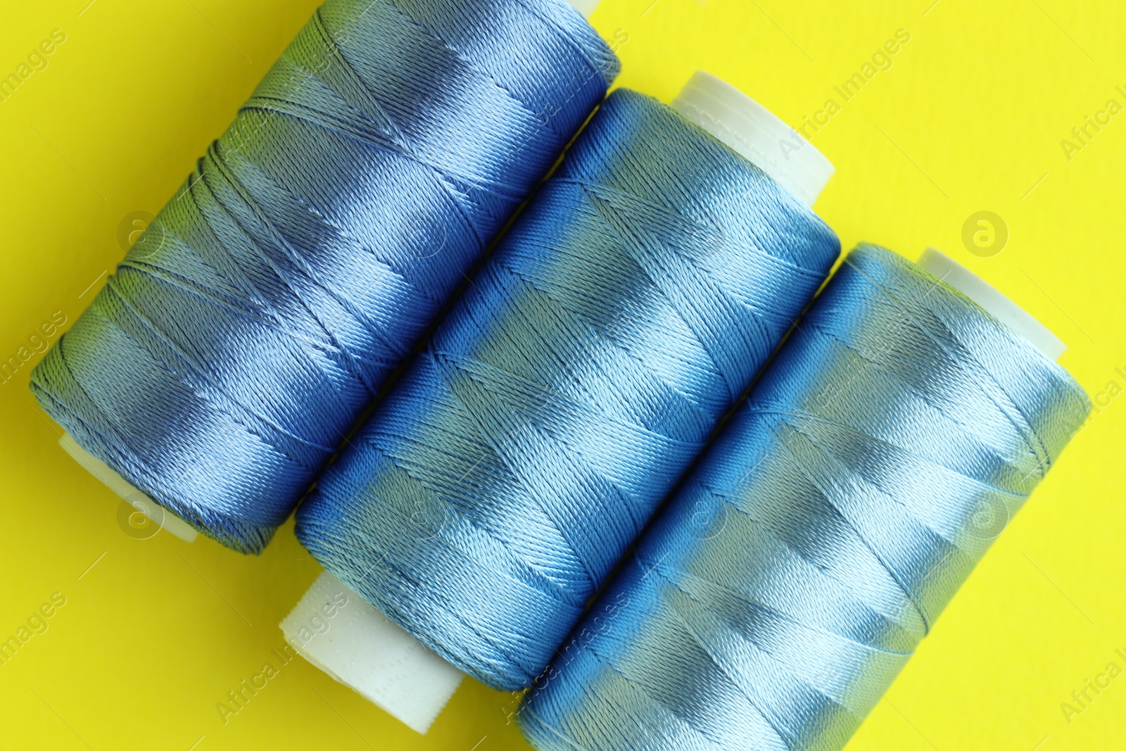 Photo of Spools of colorful sewing threads on yellow background, flat lay