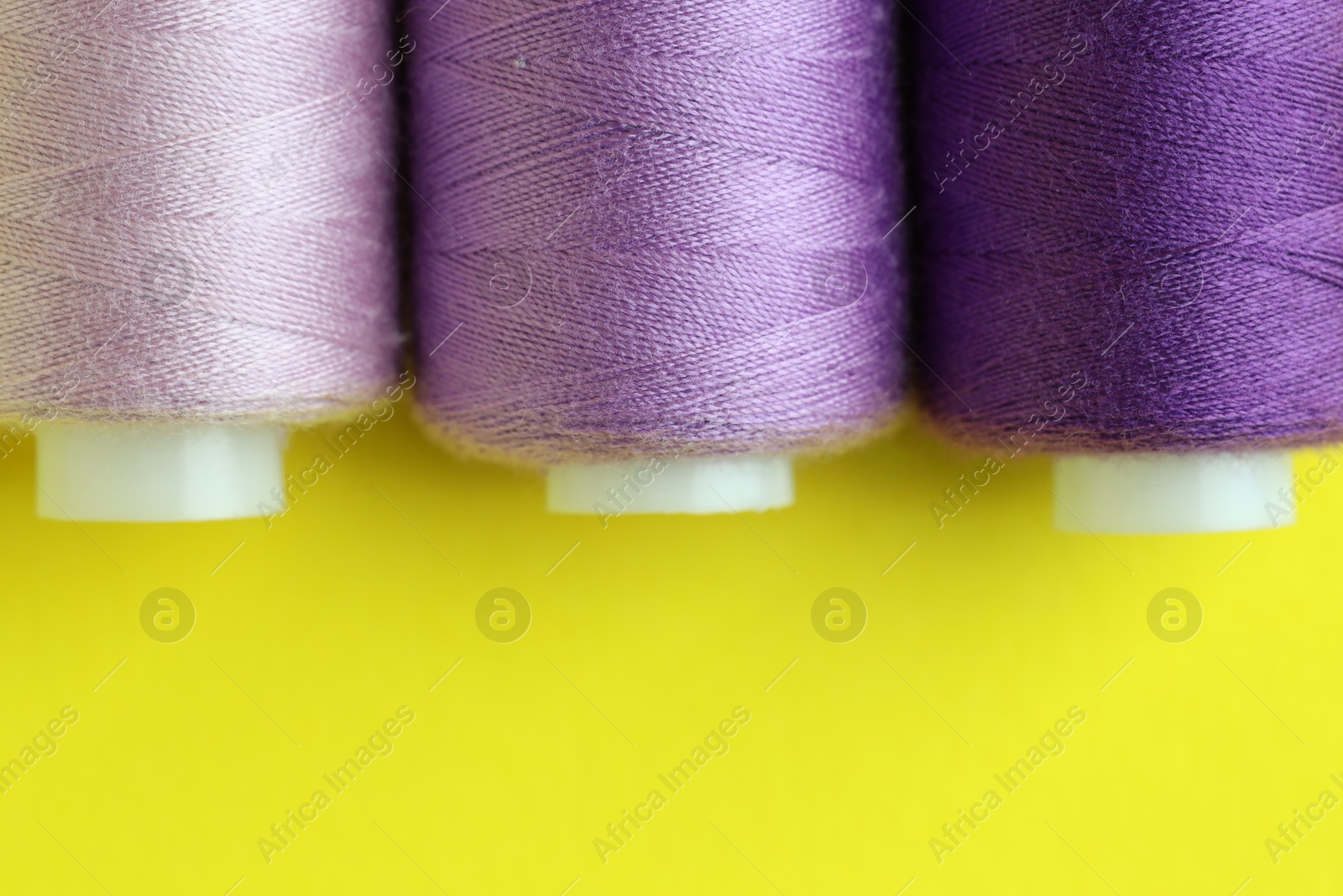 Photo of Spools of colorful sewing threads on yellow background, flat lay