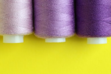 Photo of Spools of colorful sewing threads on yellow background, flat lay