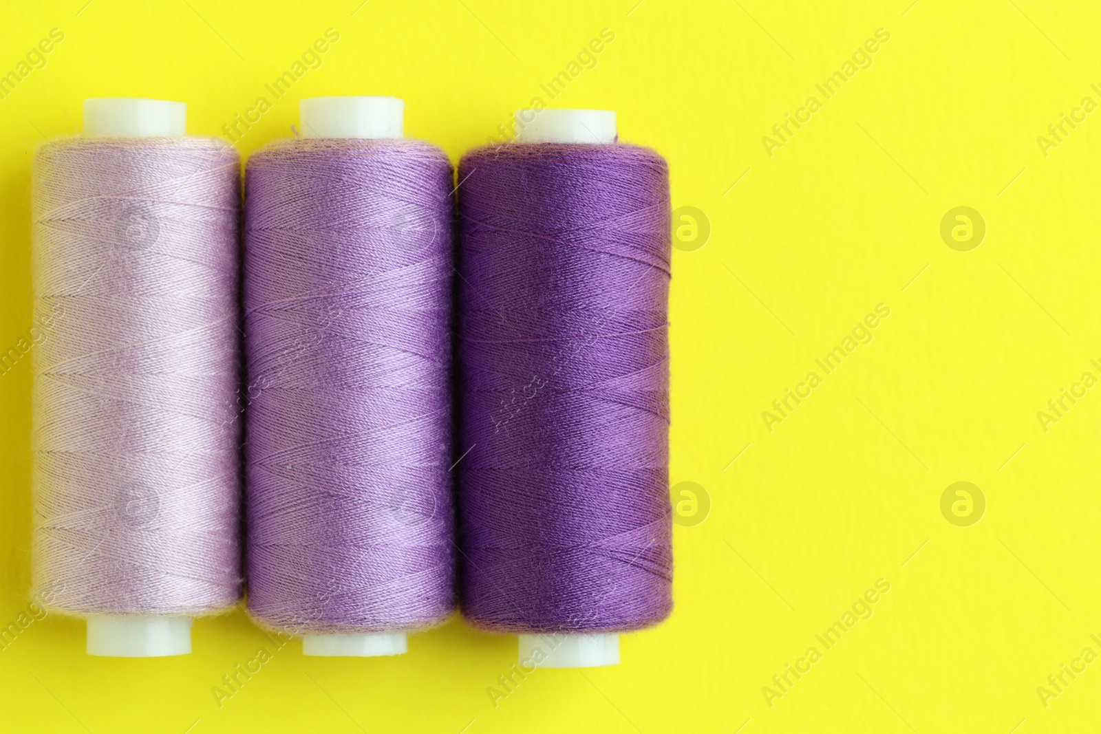 Photo of Spools of colorful sewing threads on yellow background, flat lay. Space for text