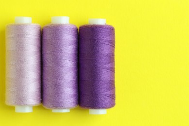 Photo of Spools of colorful sewing threads on yellow background, flat lay. Space for text