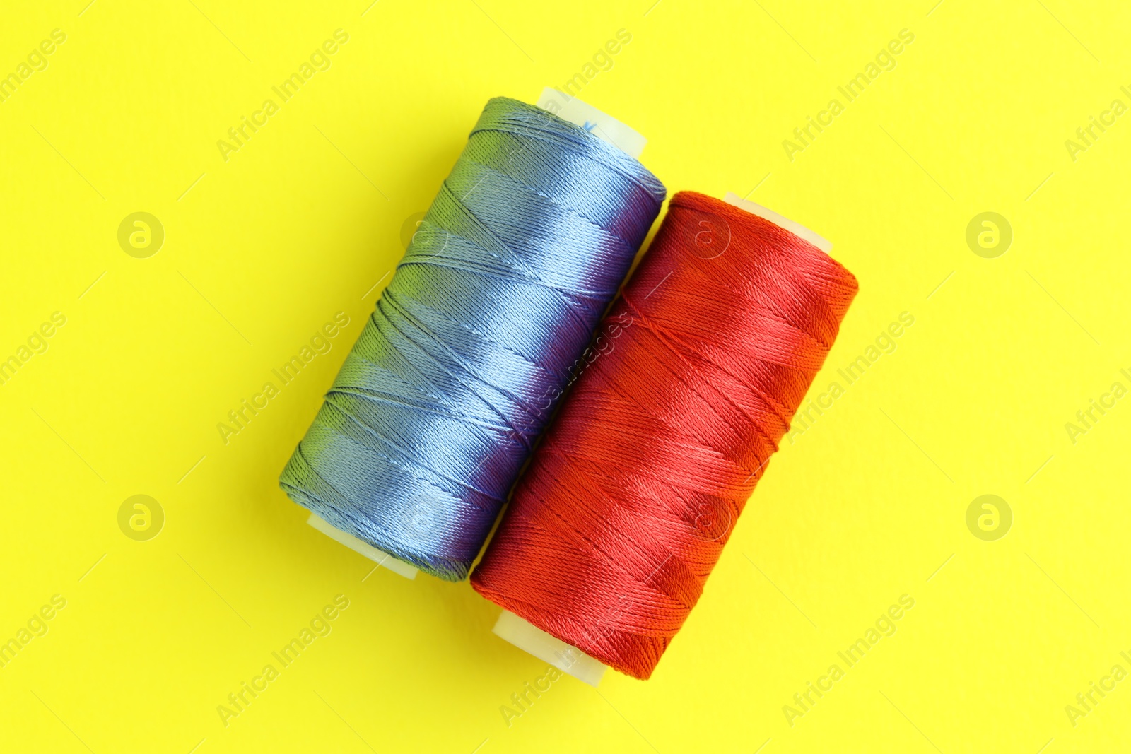 Photo of Spools of colorful sewing threads on yellow background, top view