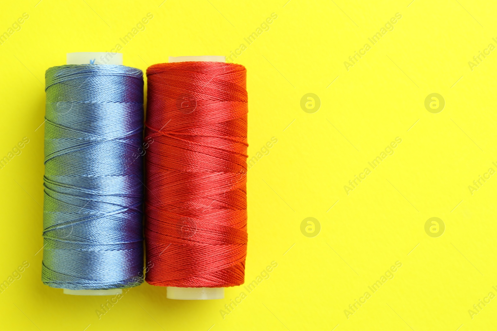 Photo of Spools of colorful sewing threads on yellow background, top view. Space for text