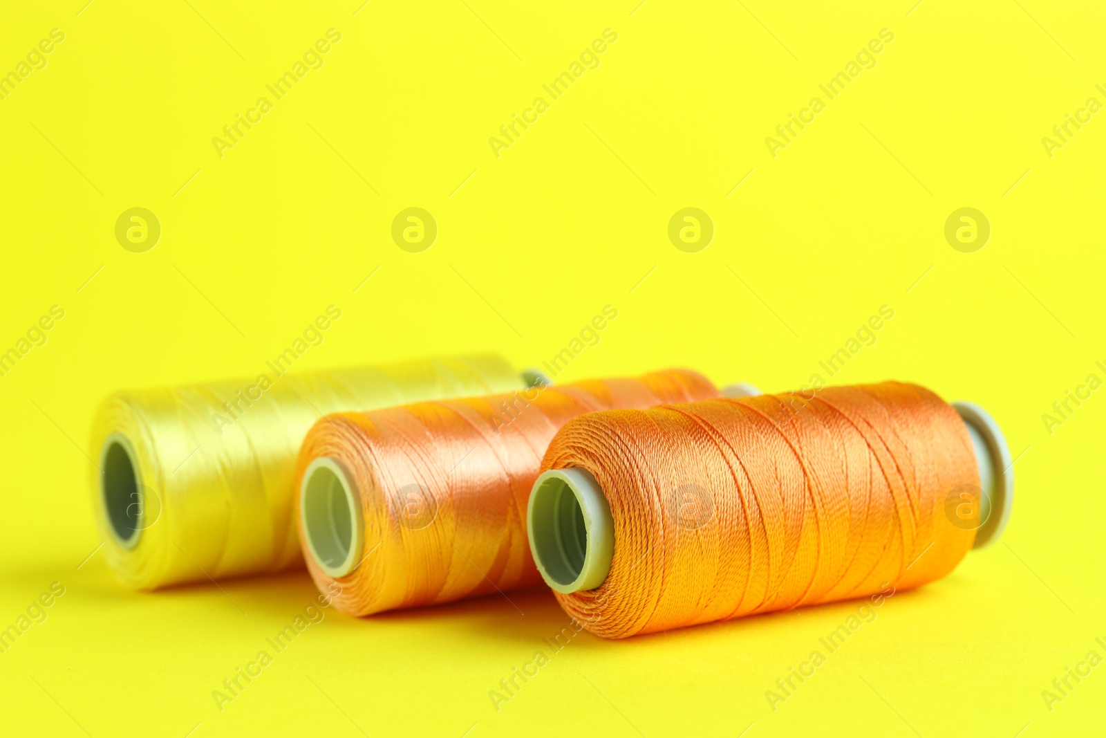 Photo of Spools of colorful sewing threads on yellow background, closeup