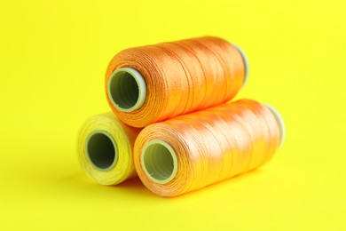 Photo of Spools of colorful sewing threads on yellow background, closeup