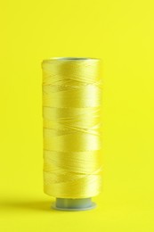 Photo of Spool of sewing thread on yellow background