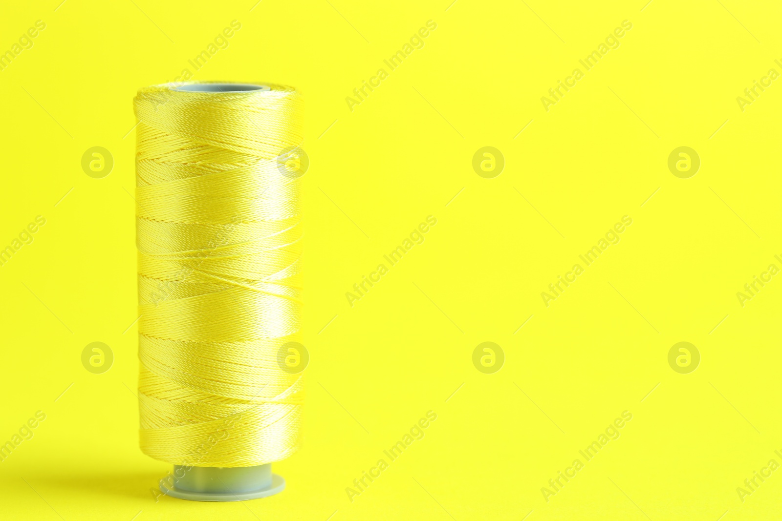 Photo of Spool of sewing thread on yellow background, space for text