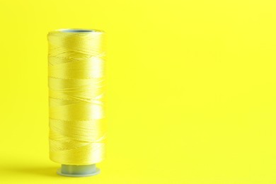 Photo of Spool of sewing thread on yellow background, space for text