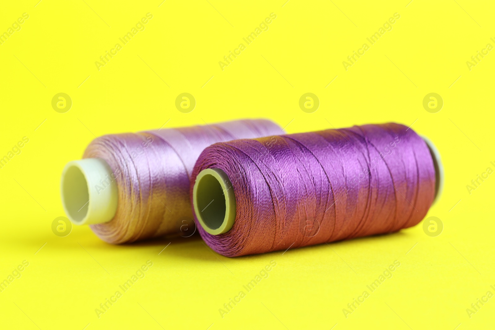 Photo of Spools of colorful sewing threads on yellow background, closeup