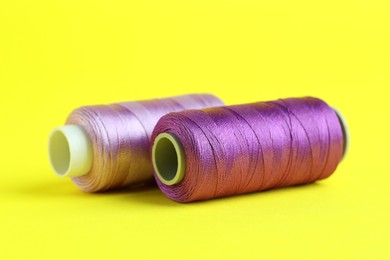 Photo of Spools of colorful sewing threads on yellow background, closeup