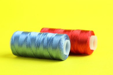 Photo of Spools of colorful sewing threads on yellow background, closeup