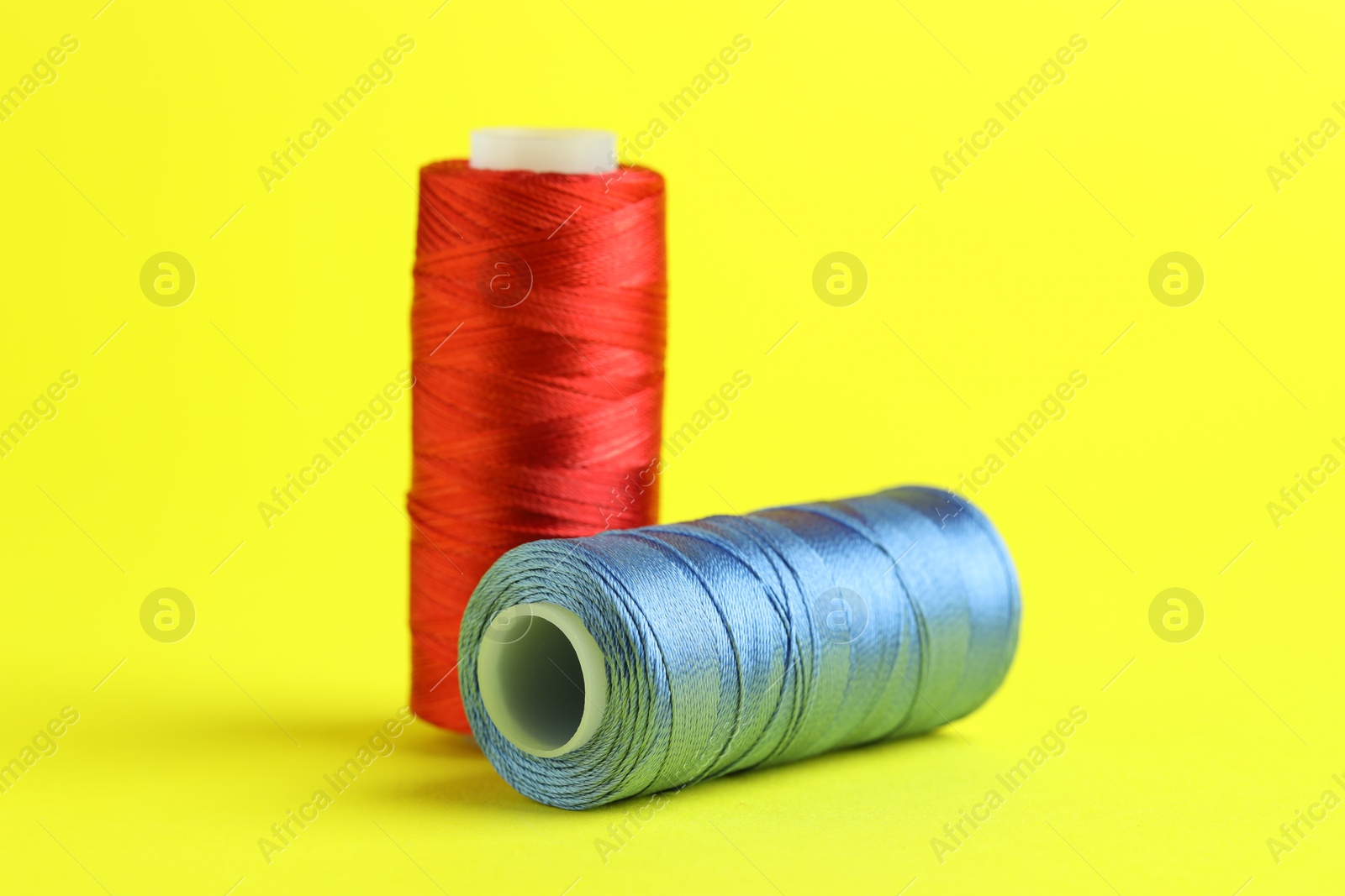 Photo of Spools of colorful sewing threads on yellow background, closeup