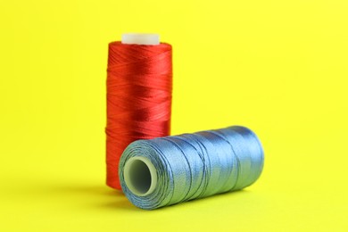 Photo of Spools of colorful sewing threads on yellow background, closeup