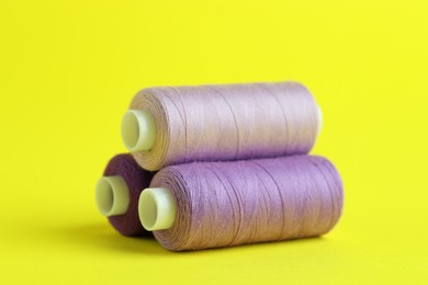 Photo of Spools of colorful sewing threads on yellow background, closeup