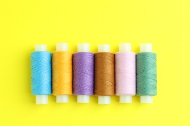 Photo of Spools of colorful sewing threads on yellow background, flat lay