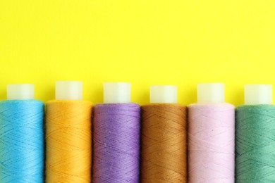 Photo of Spools of colorful sewing threads on yellow background, flat lay. Space for text