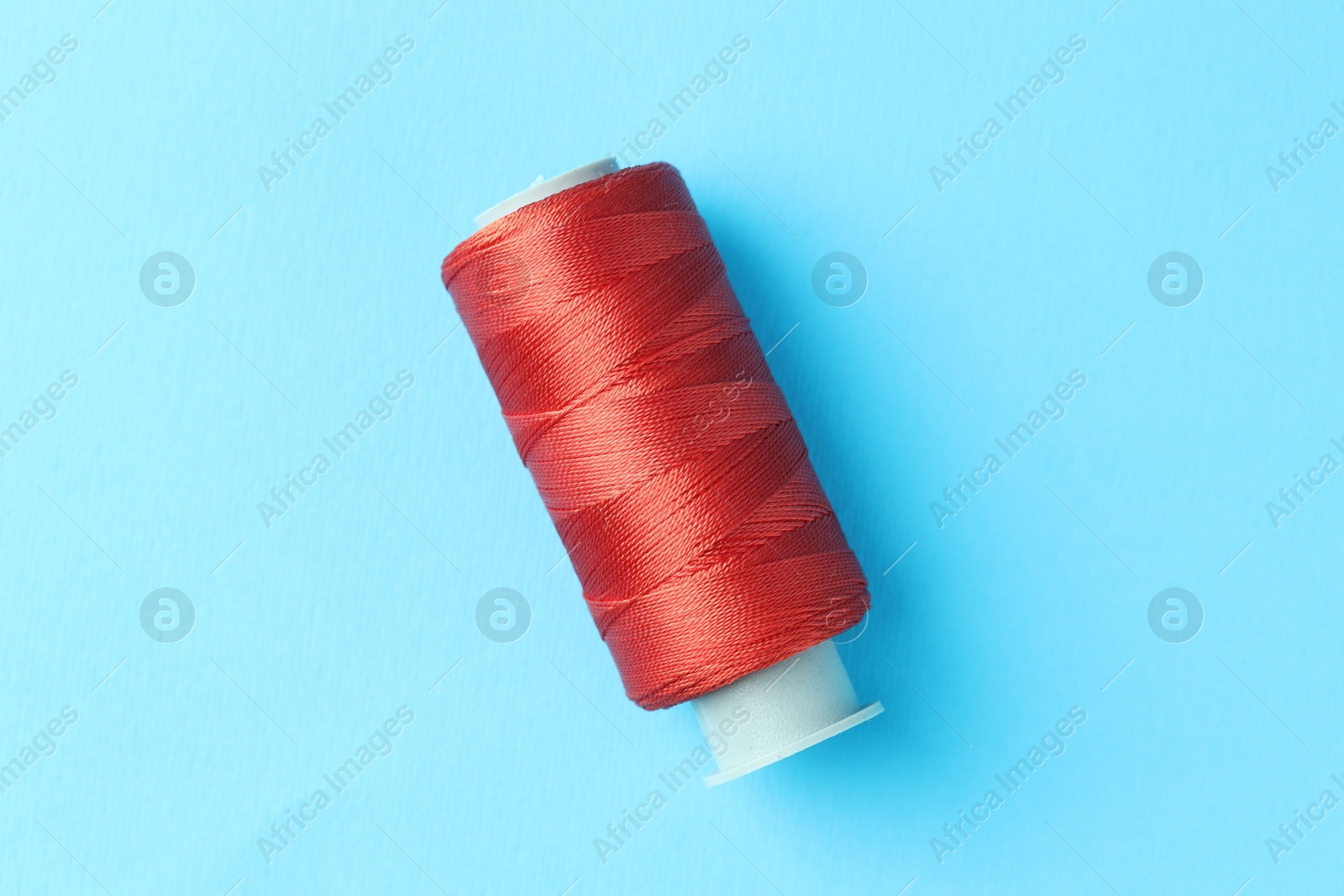 Photo of Spool of red sewing thread on light blue background, top view